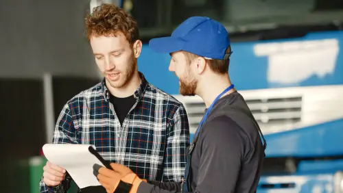 Two professionals reviewing paperwork or estimates, one wearing a plaid shirt and the other in work uniform with cap