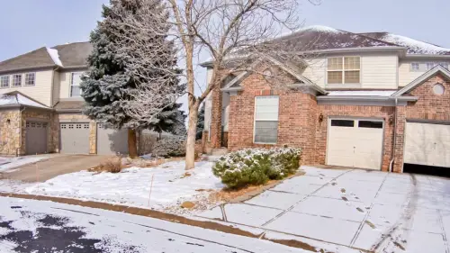 Residential home with attached garage featuring a brown garage door in winter setting with snow